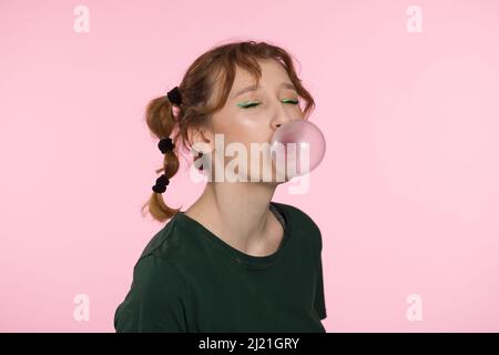 Bulle de gomme à mâcher. Jeune fille adolescente soufflant de gomme à bulles rose. Fille soufflant grande bulle isolé couleur rose fond Banque D'Images