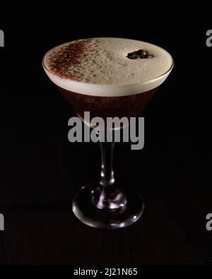 Un espresso martini mousseux, recouvert de grains de café et de poussière de chocolat sur fond noir Banque D'Images