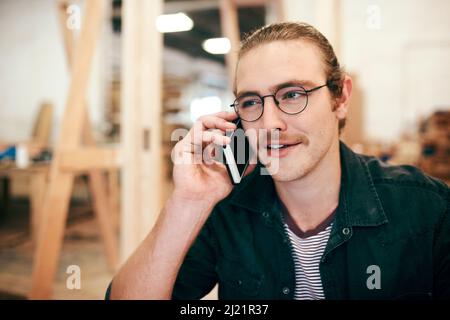 Votre commande sera livrée dans les prochains jours. Photo rognée d'un jeune menuisier faisant un appel téléphonique tout en travaillant à l'intérieur de son atelier. Banque D'Images