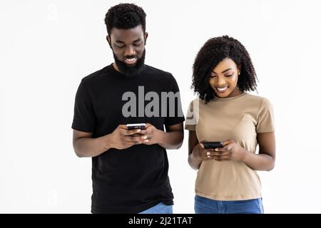 Un couple africain séduisant tient des smartphones qui s'amusent sur Internet, isolés sur fond gris de studio Banque D'Images