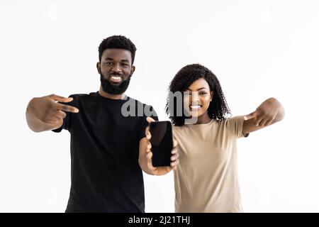 Portrait d'un couple noir excité tenant un grand smartphone avec un écran blanc en main, montrant près de l'appareil photo et pointant vers l'appareil. Gadget avec e Banque D'Images