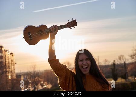 Une jeune femme latine crie avec un ukulele au-dessus de sa tête. Concept de musique et activités de loisirs Banque D'Images