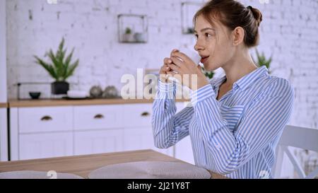 Une vue de la jeune femme portant une chemise rayée, assise dans la cuisine et buvant Banque D'Images