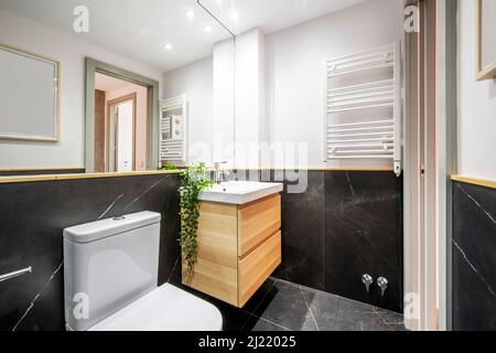 Salle de bains avec lavabo en porcelaine blanche sur meuble en bois suspendu avec deux tiroirs dans la salle de bains avec carrelage en marbre noir Banque D'Images