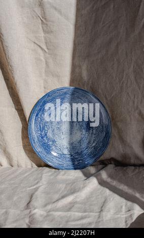 Plaque en céramique faite à la main photographiée sur du linge biologique, partiellement cachée dans l'ombre et la lumière Banque D'Images