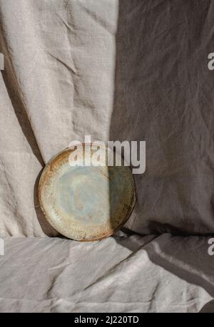 Plaque en céramique faite à la main photographiée sur du linge biologique, partiellement cachée dans l'ombre et la lumière Banque D'Images