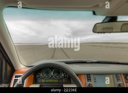 Plage et falaises vues depuis le siège conducteur d'une voiture, avec volant en premier plan. Banque D'Images