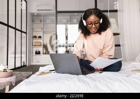 Une femme noire utilise un ordinateur portable et du papier de lecture dans la chambre Banque D'Images