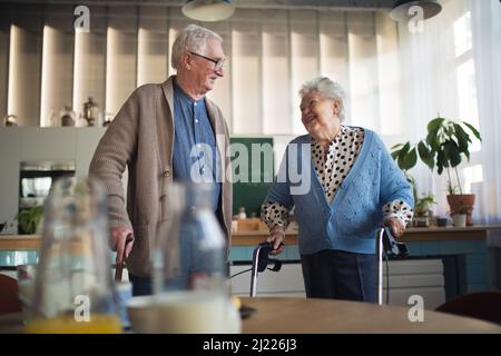 Homme et femme senior marchant avec un marcheur à l'intérieur dans l'hme de retraite de soins infirmiers. Banque D'Images