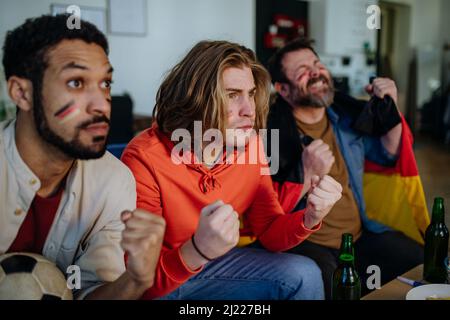 Des fans de football nerveux regardent des amis de l'équipe nationale allemande lors d'un match de football en direct à la télévision à la maison Banque D'Images