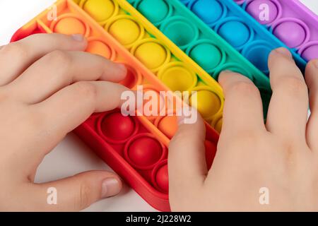 Enfant jouant avec l'arc-en-ciel pop il, appuyant les bulles avec ses doigts, vue de dessus.Nouveau jouet antistress pour les enfants et l'adulte. Copier l'espace pour le texte ou de Banque D'Images