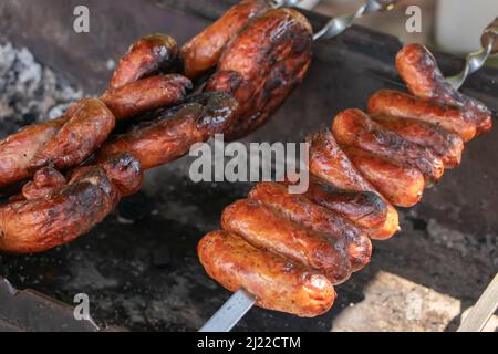 Saucisses et viande sur brochettes en bois sur le gril, gros plan Banque D'Images