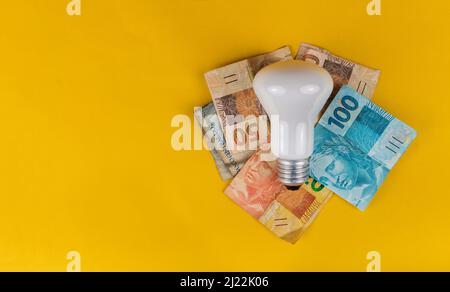 Billets de banque, pièces de monnaie, fils de fiches et ampoules isolés sur fond jaune. Banque D'Images