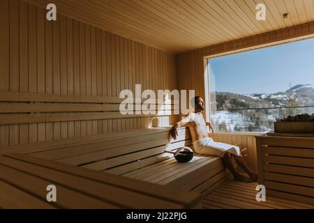 Beau jeune homme se détendant dans le sauna et regardant la forêt d'hiver par la fenêtre Banque D'Images