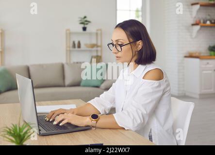 Une femme d'affaires sérieuse et sérieuse se focalise sur la saisie de courriels à l'aide d'un ordinateur portable tout en travaillant à la maison. Banque D'Images