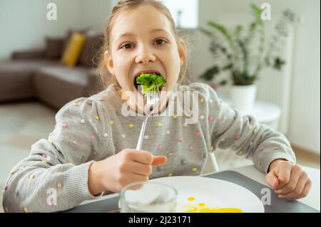 Adorable jeune fille mangeant du brocoli vert frais pendant son déjeuner Banque D'Images