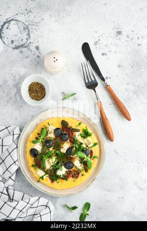 Œufs brouillés. Des œufs brouillés légers, doux et Buttery avec fromage feta, tomates séchées et olives noires sur plaque sur fond de pierre blanche. D Banque D'Images