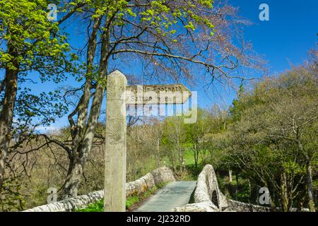 Sentier public signe de Satron, un hameau rural de Swaledale, avec 16th siècle Ivelet Bridge en arrière-plan. Printemps dans le Yorkshire Dales wi Banque D'Images