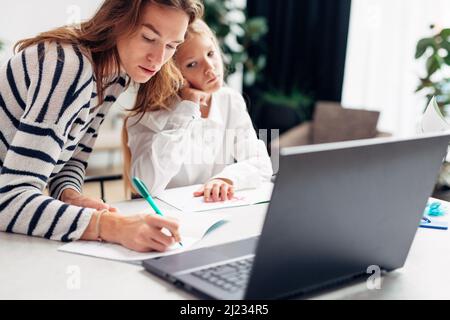 Une jeune femme écrit dans un carnet avec une fille assise à côté de son travail Banque D'Images