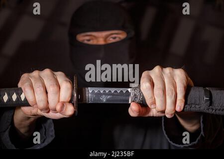 Ninja prêt à combattre, tenant une épée japonaise.Photo d'un guerrier vêtu de vêtements noirs et d'un visage fermé Banque D'Images