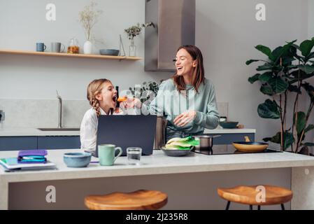 Une femme prépare un repas avec sa curieuse fille d'école à proximité. Banque D'Images