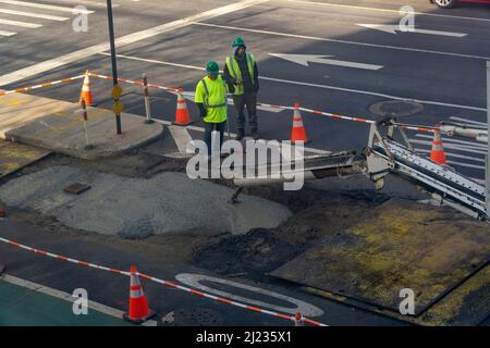 Les travailleurs versent du ciment sur une excavation de la chaussée après avoir terminé des travaux souterrains sur la neuvième avenue à Chelsea, à New York, le samedi 19 mars 2022.(© Richard B. Levine) Banque D'Images