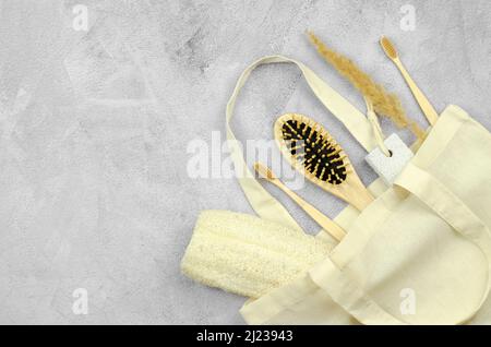 Produits de soins personnels écologiques dans un sac en lin. Brosses à dents en bambou, peigne en bois, pierre ponce et débarbouillette en toile de fond en béton Banque D'Images