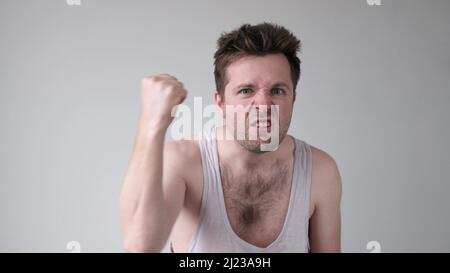 Alcoolique montrant son poing et criant avec une expression de colère, sur fond gris. Tyran familial. Allez, attaquez, je vous batterai. Banque D'Images