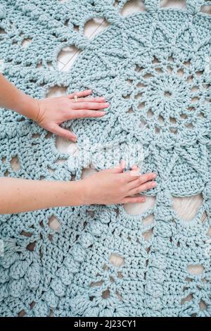 Les mains des femmes reposent sur un tissu écossais de laine tricotée grossière sur un parquet, vue du dessus. Moquette faite à la main Banque D'Images