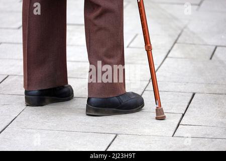 Homme avec un bâton de marche dans une rue, les jambes de sexe masculin dans un pantalon sur le trottoir. Concept de handicap, personne qui se limite Banque D'Images