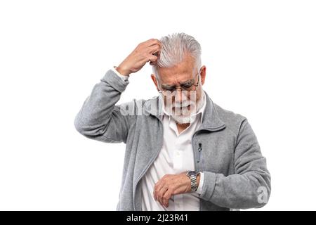 Un homme vieux et élégant, aux cheveux gris et avec une barbe, égratignure sa tête et regarde sa montre. Le concept de ponctualité et de discipline. Banque D'Images