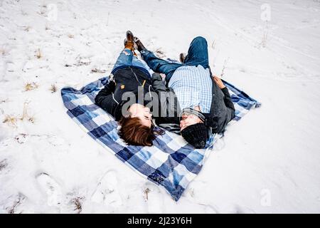 Homme et femme allongé sur une couverture à carreaux bleus entourée de neige Banque D'Images
