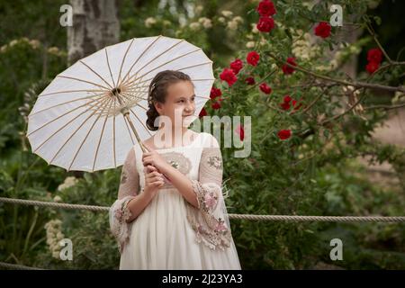 Communion fille posant avec un parapluie blanc dans un parc Banque D'Images