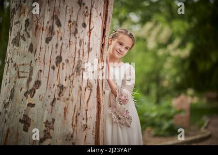 Communion fille posant à côté d'un grand arbre dans un parc Banque D'Images