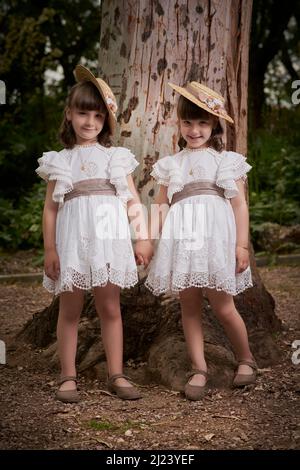 Communion jumelle petites sœurs à côté d'un grand arbre dans un parc Banque D'Images