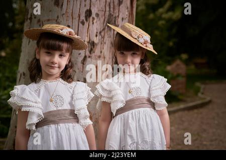 Communion jumelle petites sœurs à côté d'un grand arbre dans un parc Banque D'Images