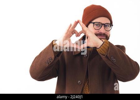 Portrait d'un jeune homme caucasien barbu en lunettes et chapeau souriant et montrant le coeur geste avec ses mains hippster brun décontracté vêtements isolés blanc fond studio tourné . Photo de haute qualité Banque D'Images