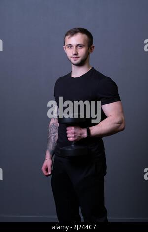 Un type avec des haltères dans un T-shirt noir musclé homme sport posant, pour le gris vieilli de l'homme et de la tenue d'entraînement, attrayant t. Maillot de levage, gymnase Banque D'Images