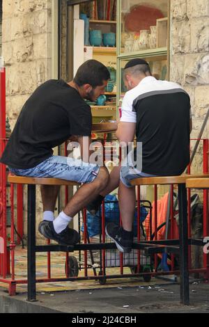 Deux jeunes hommes se concoupent en étant assis sur le trottoir à Jérusalem, en Israël. Banque D'Images