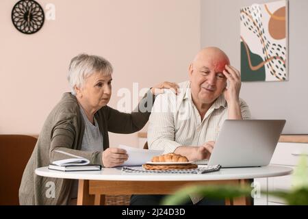 Homme âgé souffrant de maux de tête et sa femme payant des factures à la maison Banque D'Images