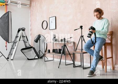 Photographe masculin avec appareil photo assis dans une chaise près du mur rose dans un studio moderne Banque D'Images