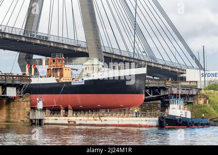 30 mars 2022, Glebe Island Bridge, Sydney, Australie : le navire à vapeur côtier de 1927, John Oxley ayant subi des années de restauration et de préservation, est photographié ici sur le chemin d'être finalement renfloué après 21 ans montés sur un ponton aux ateliers de la Sydney Heritage Fleet à Roselle Bay. Après avoir facilement dégagé l'immense pont ANZAC en béton, le ponton passe par l'ouverture de l'ancien pont Glebe Island sur son chemin vers un quai sec à Garden Island, plus loin en bas du port de Sydney où il sera soigneusement rénové et testé. Banque D'Images