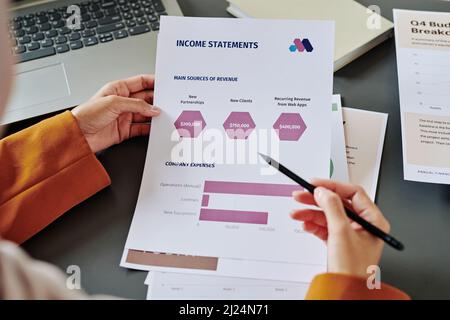 Les mains de la jeune femme comptable pointant vers un document avec des diagrammes et des diagrammes financiers tout en analysant ou en présentant des informations Banque D'Images