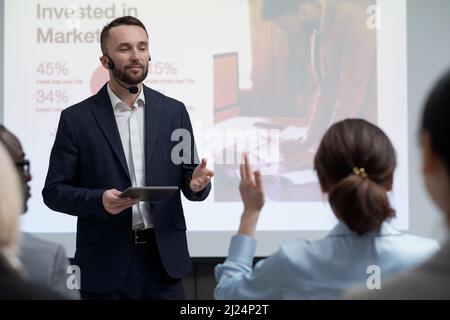 Jeune homme d'affaires contemporain pointant vers l'un de ses collègues lors de la présentation des revenus investis dans le marketing lors de la conférence Banque D'Images