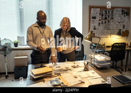 Deux agents interraciaux du FBI formulant des suggestions sur la recherche de chef de gang tout en regardant à travers les données personnelles des criminels Banque D'Images