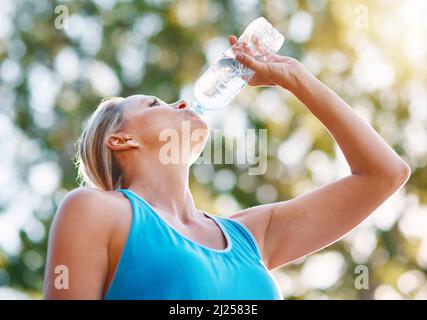 Restez toujours hydraté pendant vos entraînements. Photo d'une femme mature qui boit de l'eau hors d'une bouteille à l'extérieur. Banque D'Images