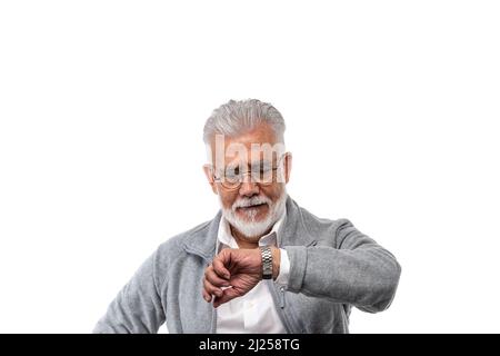 Un homme âgé élégant aux cheveux gris et à la barbe sur fond blanc isolé regarde sa montre. Le concept de ponctualité et de discipline. Banque D'Images