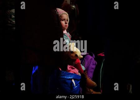 Une jeune fille d'Ukraine est assise dans une valise dans une file d'attente alors que les réfugiés ukrainiens attendent dans la file d'attente pour monter dans un train pour rentrer en Ukraine, à l'extérieur de la gare de Przemysl Glowny, dans l'est de la Pologne, après avoir fui l'invasion russe de l'Ukraine. Date de la photo: Mardi 29 mars 2022. Banque D'Images