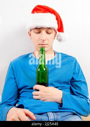 Jeune homme malheureux à Santa Hat avec une bouteille de bière près du mur dans la chambre Banque D'Images