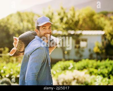 Je n'ai pas peur de me salir les mains. Portrait d'un jeune fermier heureux portant un sac de compost sur son épaule sur la ferme. Banque D'Images